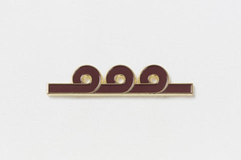 A rectangular maroon pin with gold edges and three upward loops in the design in the center