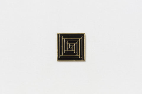 A square black pin with gold edges throughout a geometric vortex