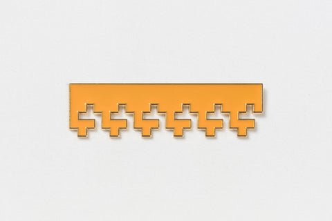 a rectangular orange pin with gold edges and Greek key designs descending