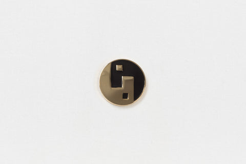 A round black and gold pin with a geometric yin yang