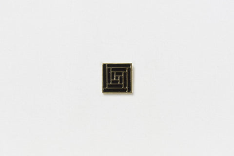 A square black pin with gold edges throughout a geometric vortex